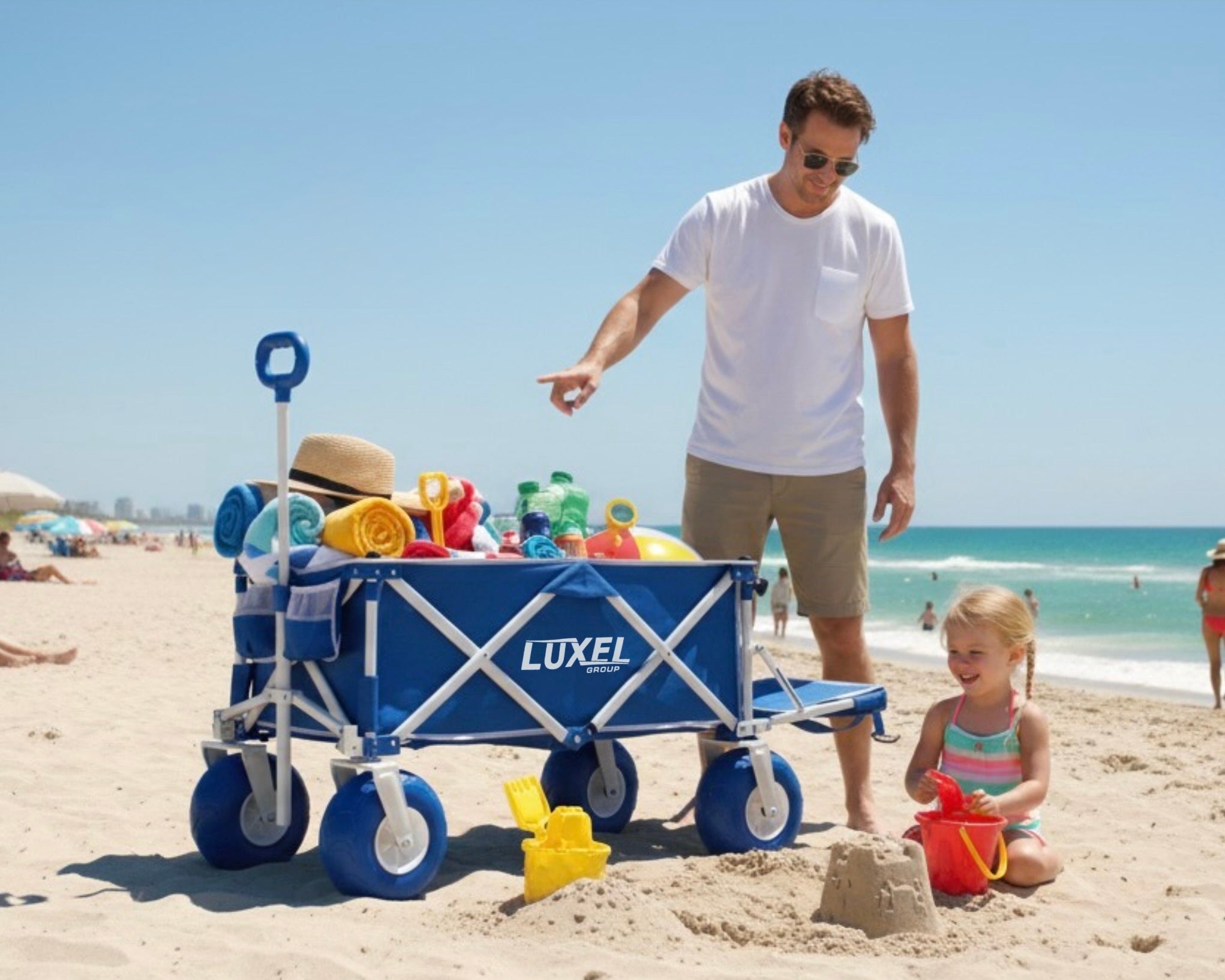 Man and child with a Luxel beach cart filled with toys on a sandy beach.