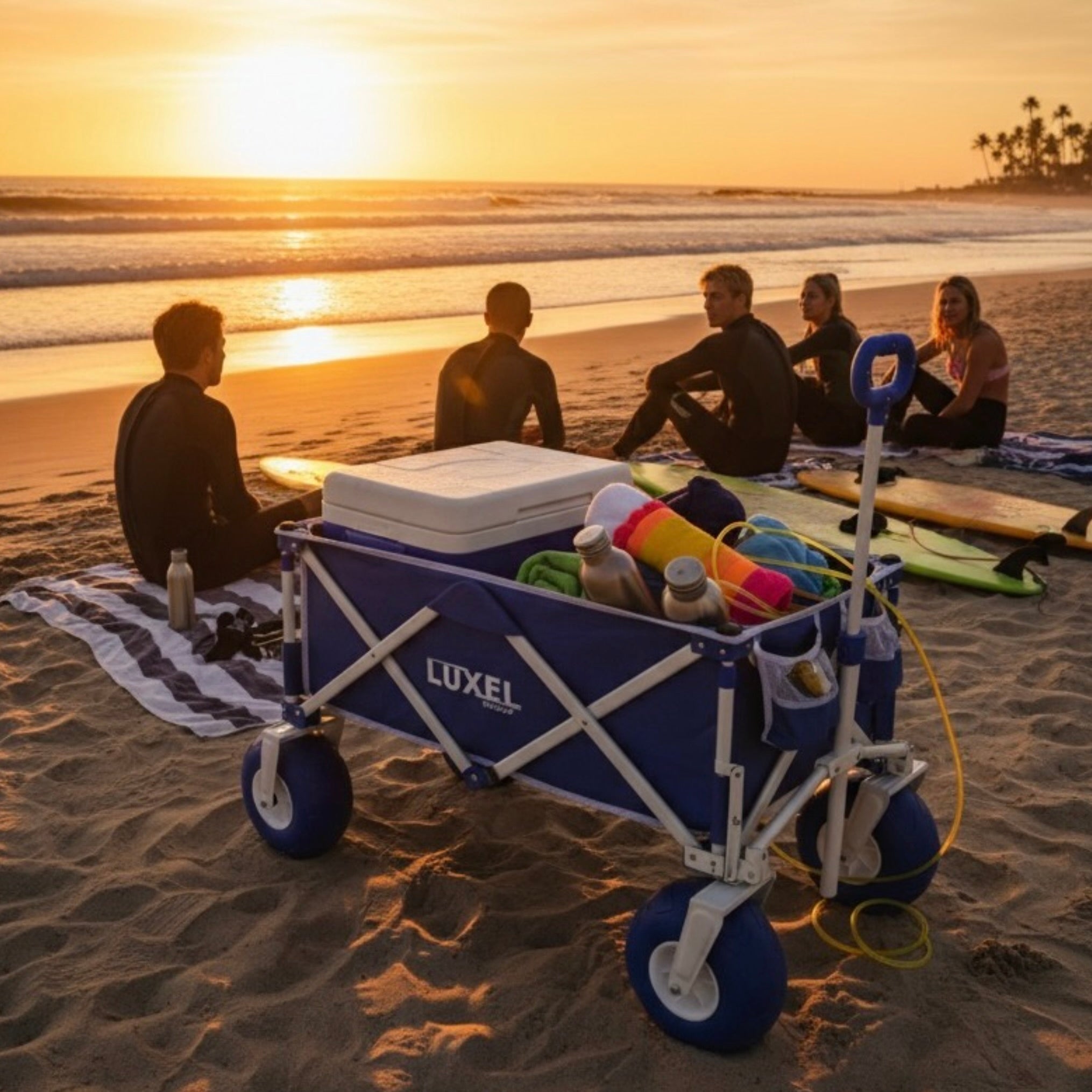 Blue LUXEL beach cart with cooler and beach gear on a sandy beach at sunset.