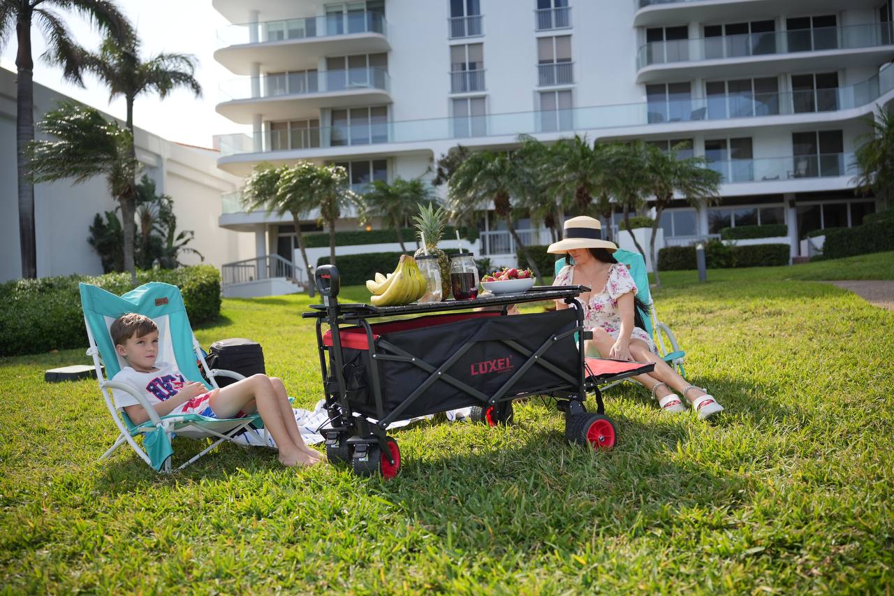 Luxel Group electric folding wagon with tabletop in use as a picnic table between two people relaxing on a lawn.